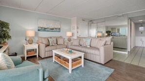 A living room with striped sofas, a white coffee table, and a painting of sailboats. - Thunder Island 161d 2 Bedroom Condo (Ocean City)