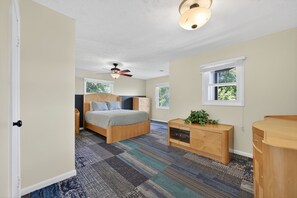 Een slaapkamer met een bed, nachtkastje, dressoir, plafondventilator en een raam.