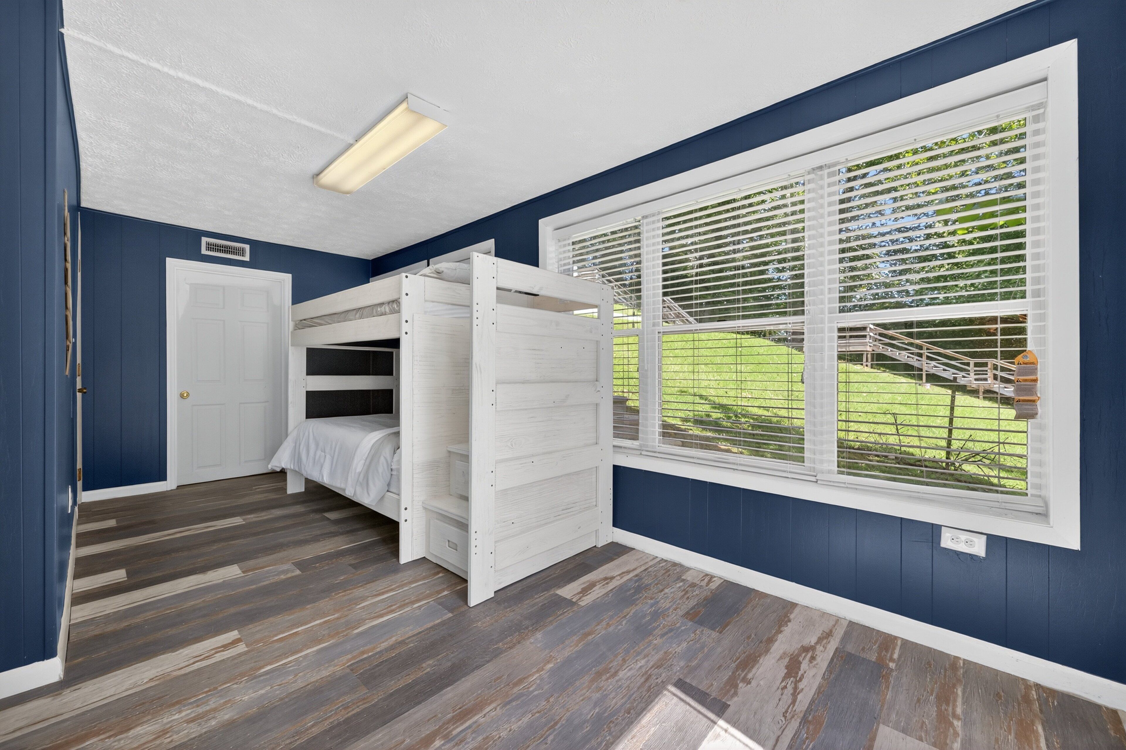 A room with a bunk bed, a window with blinds, a door, and a ceiling light.