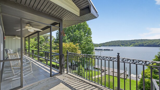 A covered balcony with a view of a lake, a rocking chair, and a metal railing. - Lakefront Getaway With Private Dock & Scenic Views 3 Bedroom Home (Kingsport)