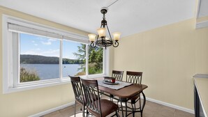 A dining area with a table and chairs, a chandelier, and a view of a lake through large windows. - Lakefront Getaway With Private Dock & Scenic Views 3 Bedroom Home (Kingsport)