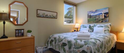 A bedroom with a bed, a dresser, a mirror, a window, and a painting on the wall.
