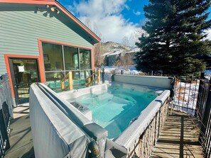 A hot tub area with a stone wall, a wooden deck, and a building with large windows and a red door. - Telluride Lodge 324 1 Bedroom Studio (Telluride)