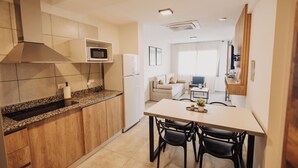 A compact kitchen with a microwave, stove, and sink. There is a dining area with a table and chairs. - Edificio Coirón Premium (San Rafael)