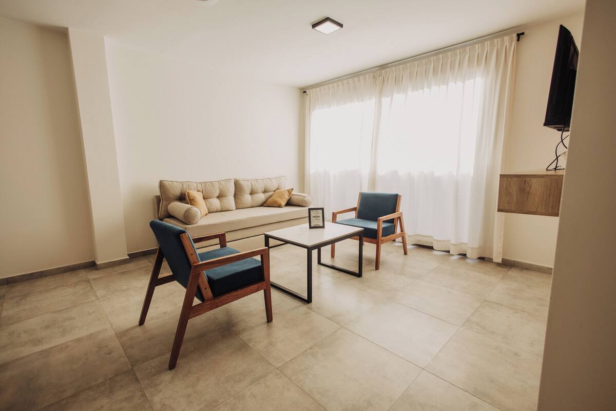 A living room with a sofa, two armchairs, a coffee table, and a TV mounted on the wall.