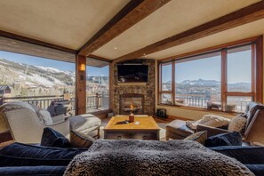 A cozy living room with a stone fireplace, comfortable seating, and a large window offering a mountain view. - One-Level See Forever by InvitedHome | Deck, Walk to Festivals, Developer’s Unit (Mountain Village)