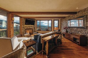 A spacious living room with a stone fireplace, a large window offering a mountain view, and a cozy seating area.