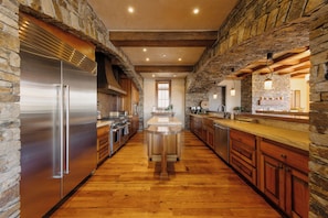 A kitchen with a central island, stone walls, wooden beams, and stainless steel appliances. - One-Level See Forever by InvitedHome | Deck, Walk to Festivals, Developer’s Unit (Mountain Village)