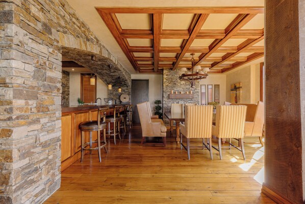 A spacious kitchen with a stone wall, wooden ceiling beams, and a bar area with stools.