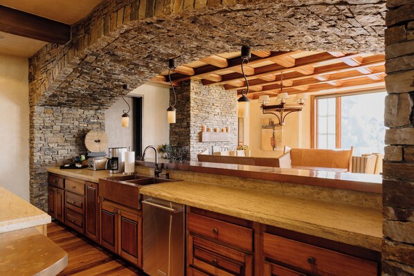 Una cocina con pared de piedra, armarios de madera, lavavajillas integrado e iluminación colgante.
