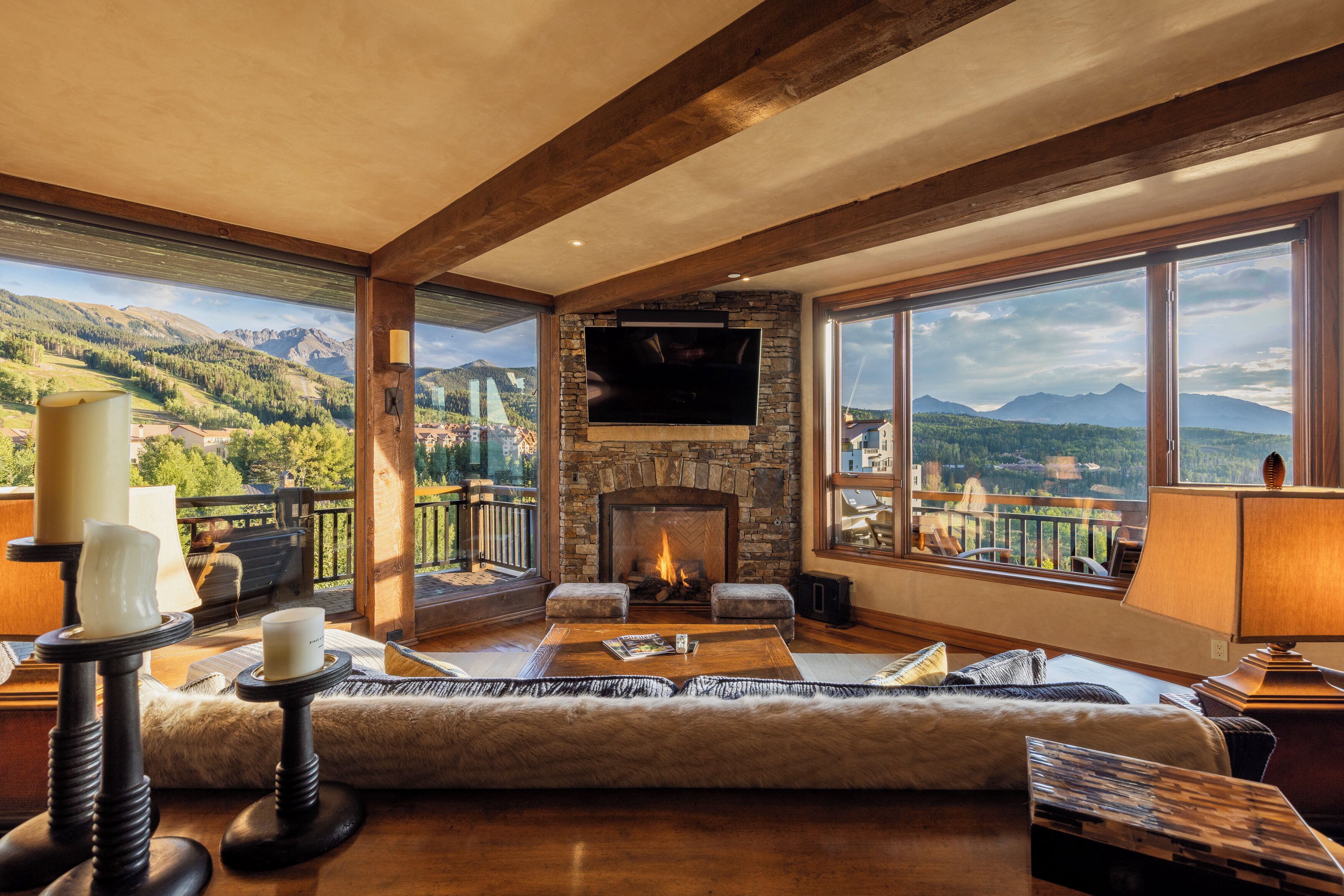 A spacious living room with a stone fireplace, a flat-screen TV, and a large window offering a mountain view.