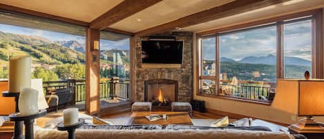 Amplia sala de estar con chimenea de piedra, televisor de pantalla plana y ventana grande con vistas a la montaña.