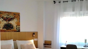 A hotel room with a bed, a desk, a chair, and a painting on the wall.
