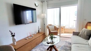 A modern living room with a flat-screen TV, a glass coffee table, a sofa, and a chair.