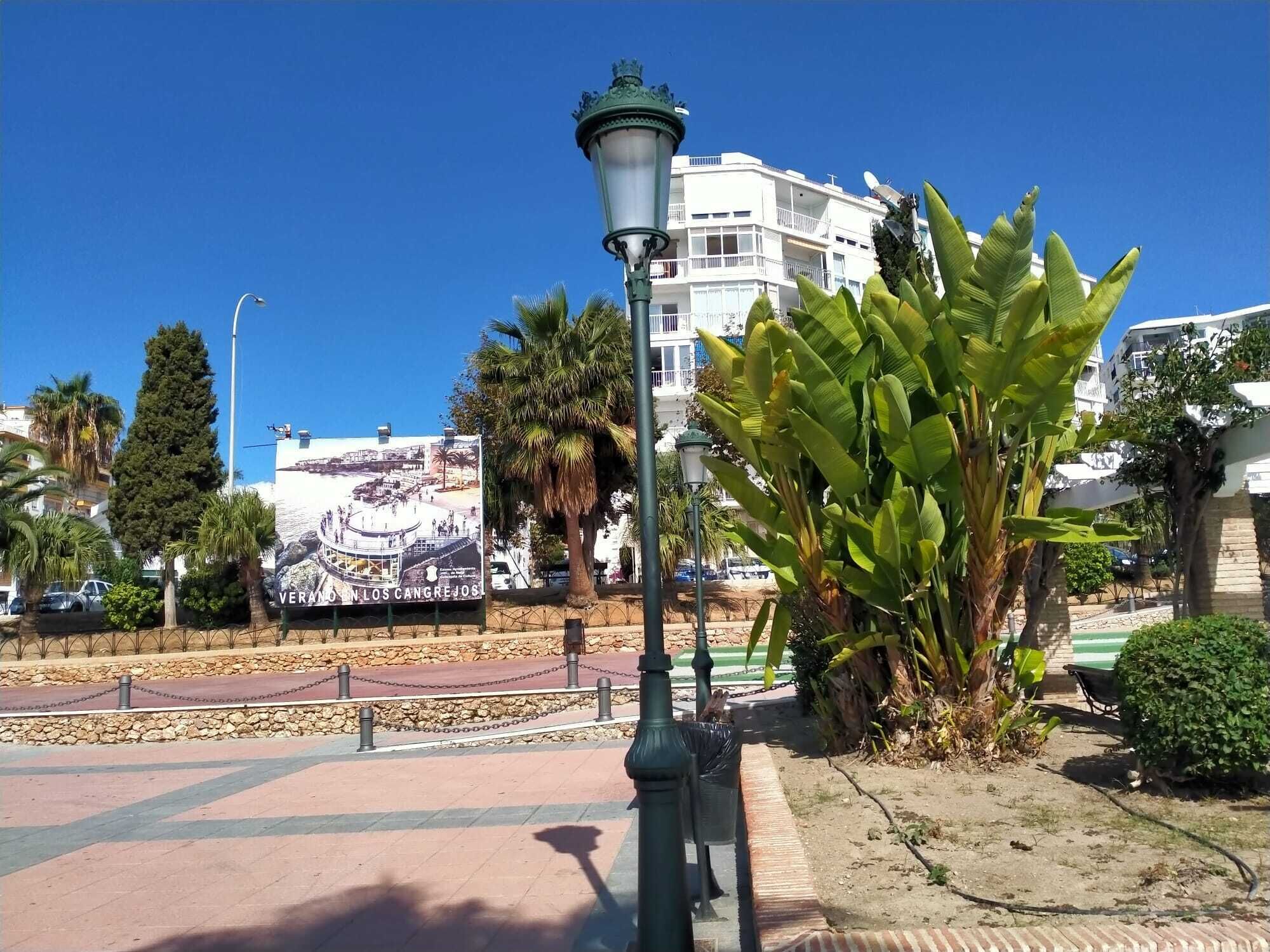 Escena callejera con un cartel grande, una farola y una palmera.