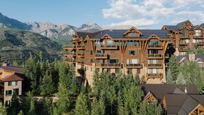 A multi-story log cabin-style building with multiple balconies and large windows, surrounded by trees and mountains. - See Forever Home by InvitedHome | Walk to Ski, Ski Valet, Large Deck with Views (Telluride)