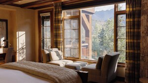 A hotel room with a large bed, a desk with a chair, two armchairs, and a view of mountains through large windows. - See Forever Home by InvitedHome | Walk to Ski, Ski Valet, Large Deck with Views (Telluride)