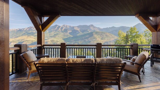 A covered outdoor seating area with wooden furniture and a view of mountains. - See Forever Home by InvitedHome | Walk to Ski, Ski Valet, Large Deck with Views (Telluride)