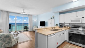 A modern kitchen with a view of the ocean, a dining area with a view, and a living room with a large window. - Celadon condo - beach access, pools and hot tub (Panama City Beach)