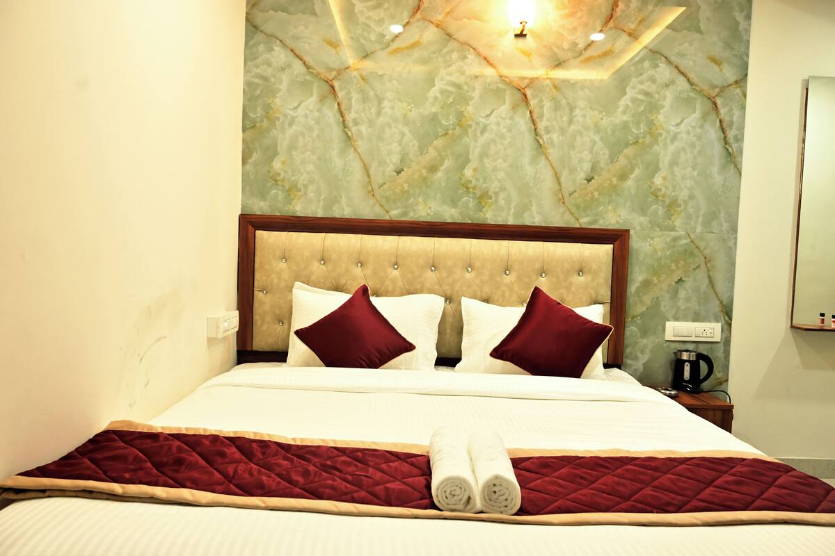 Una cama bien hecha con un edredón rojo acolchado, dos almohadas y un par de toallas enrolladas.