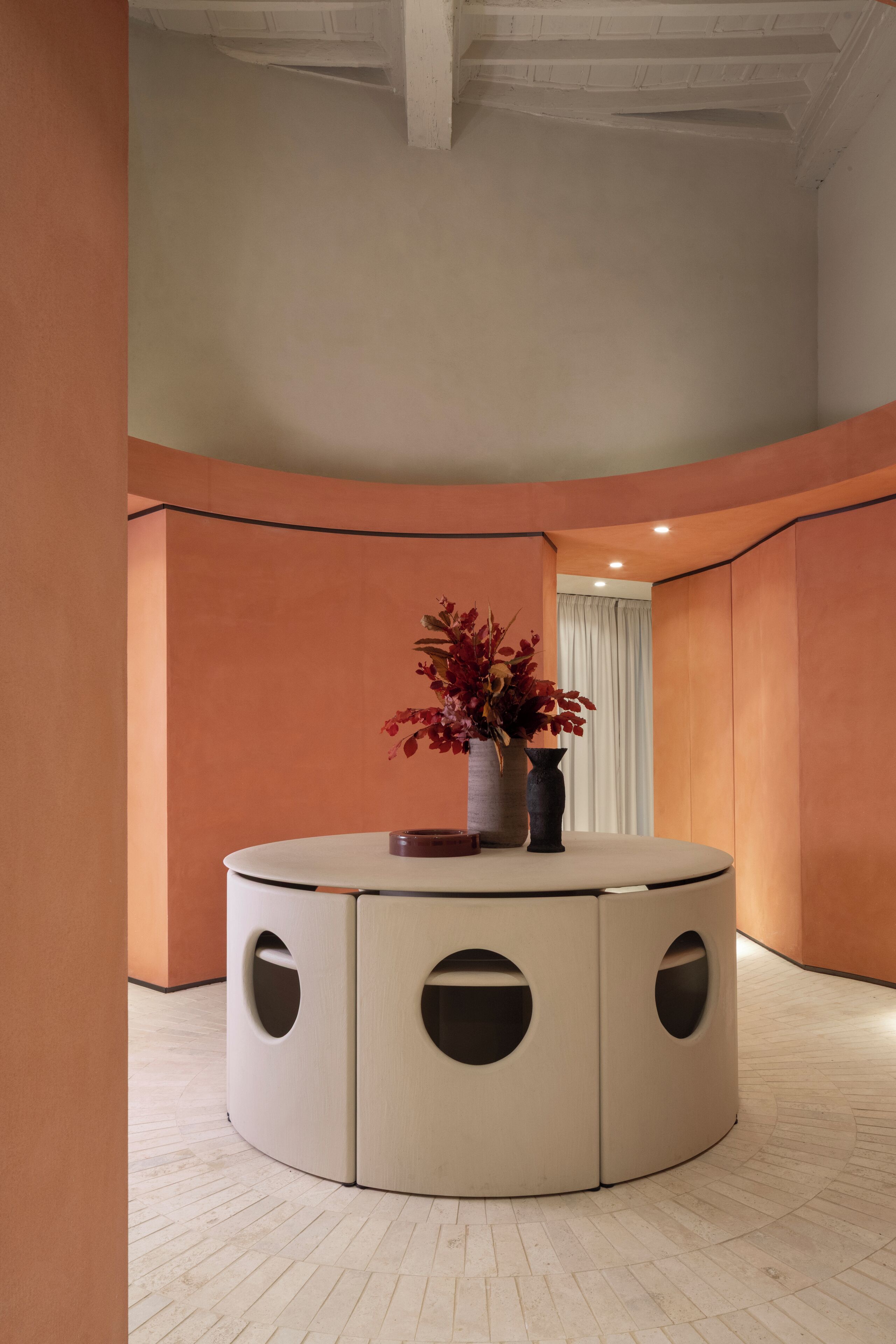 A circular seating area with a vase of red flowers on a table, surrounded by walls with a curved design.