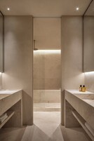 Un bagno moderno con zona doccia centrale, scaffalature integrate e due lavabi con articoli da toilette.