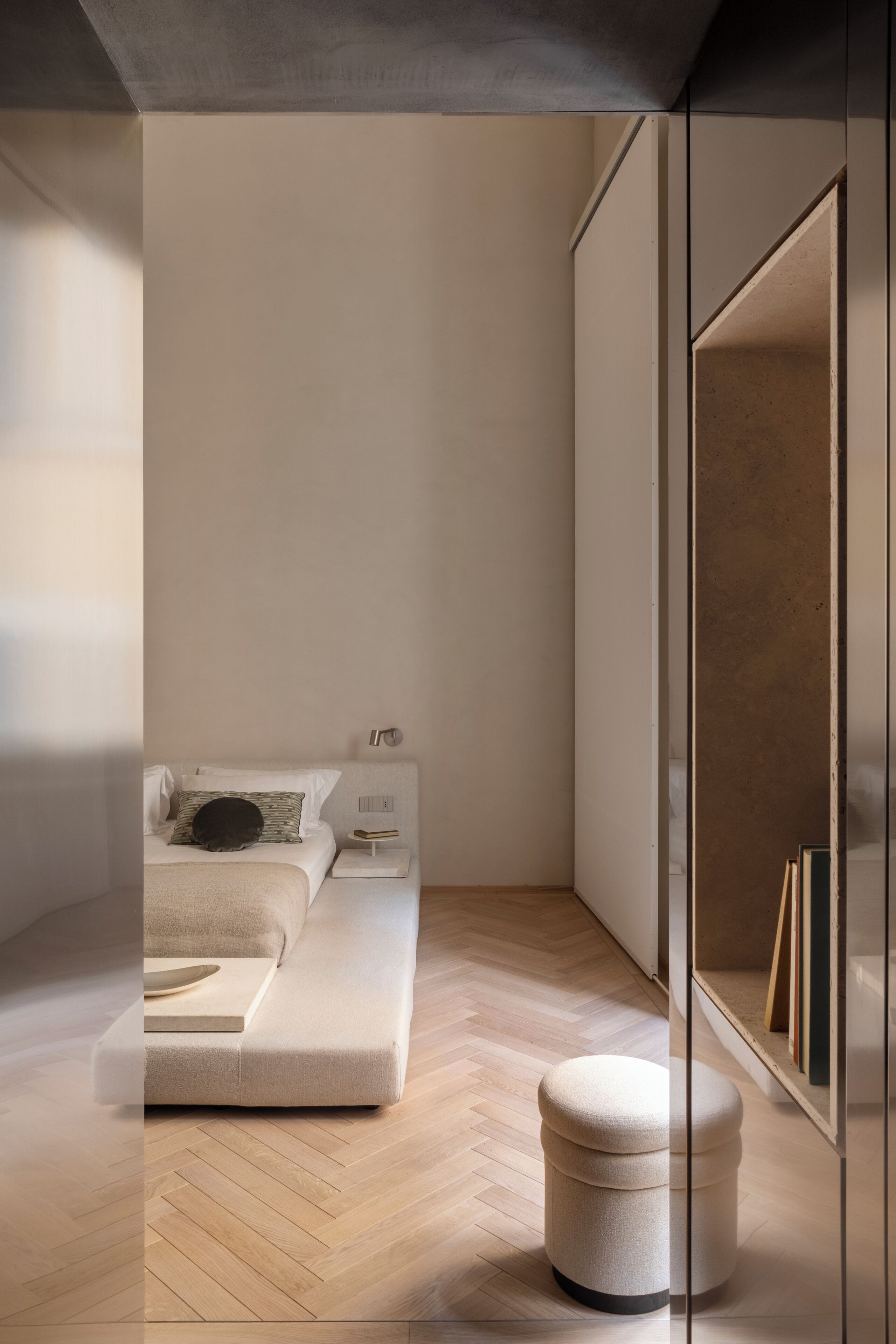 Un dormitorio moderno con sofá cama, una mesita de noche pequeña y un otoman redondo.