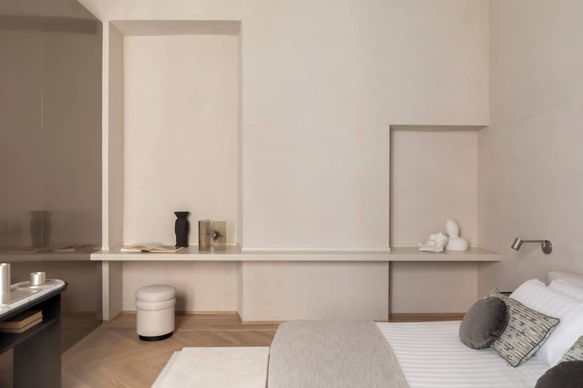 A minimalist bedroom with a bed, bedside table, and a small stool.