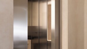 A modern room with a minimalist design, featuring a sleek black chair with a round cushion, a small round table with a white napkin, and a large metallic panel wall. - Hotel Trame (Rome)