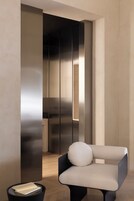 Una stanza moderna dal design minimalista, con una elegante sedia nera dotata di cuscino rotondo, un tavolino piccolo con tovagliolo bianco e un'ampia parete rivestita in metallo.