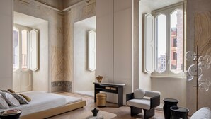 A modern bedroom with a large bed, a desk, a chair, and a view of the city through large windows. - Hotel Trame (Rome)
