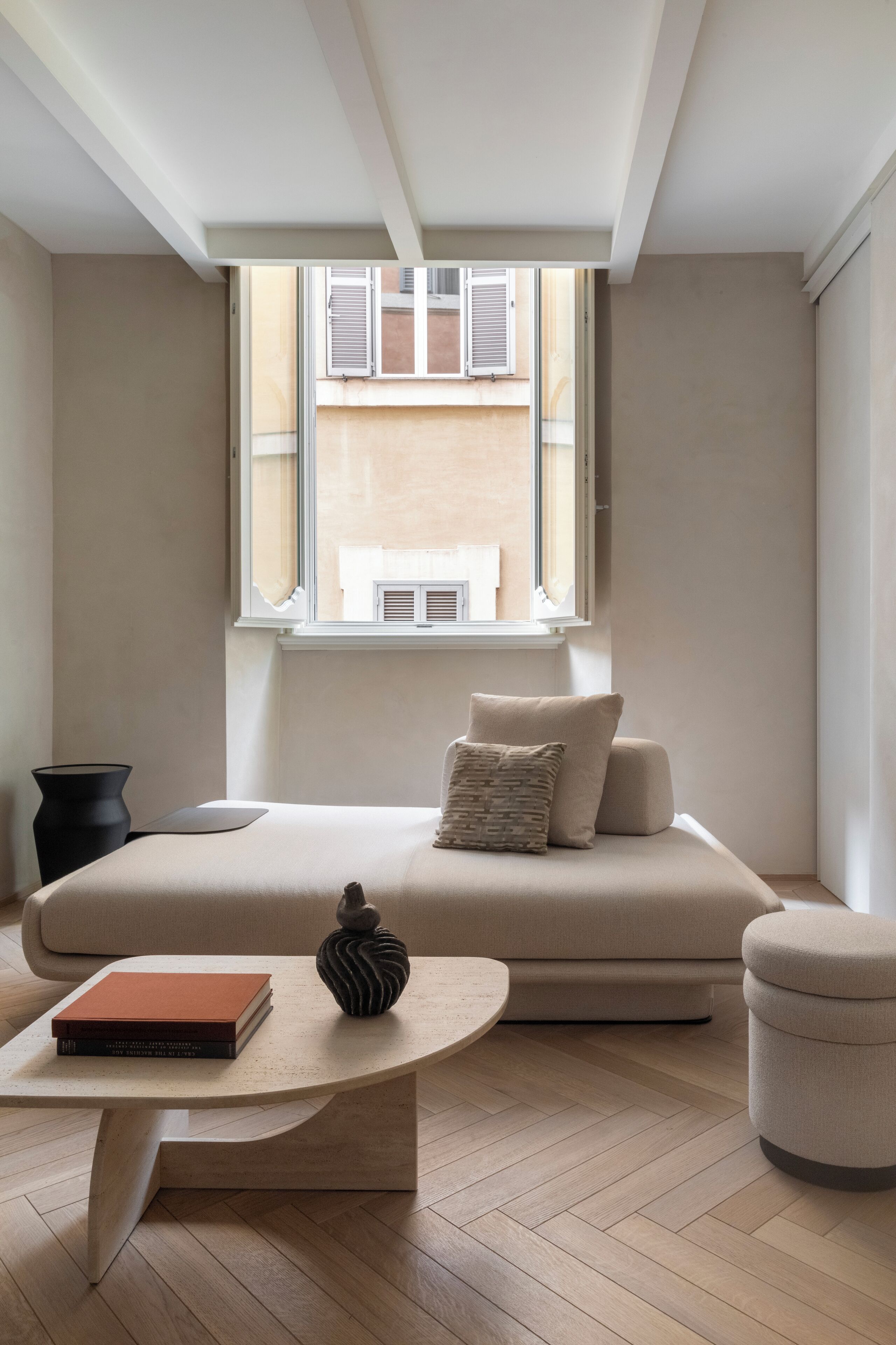 A minimalist bedroom with a bed, a small table, and a window with shutters.