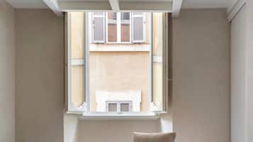 A minimalist bedroom with a bed, a small table, and a window with shutters.