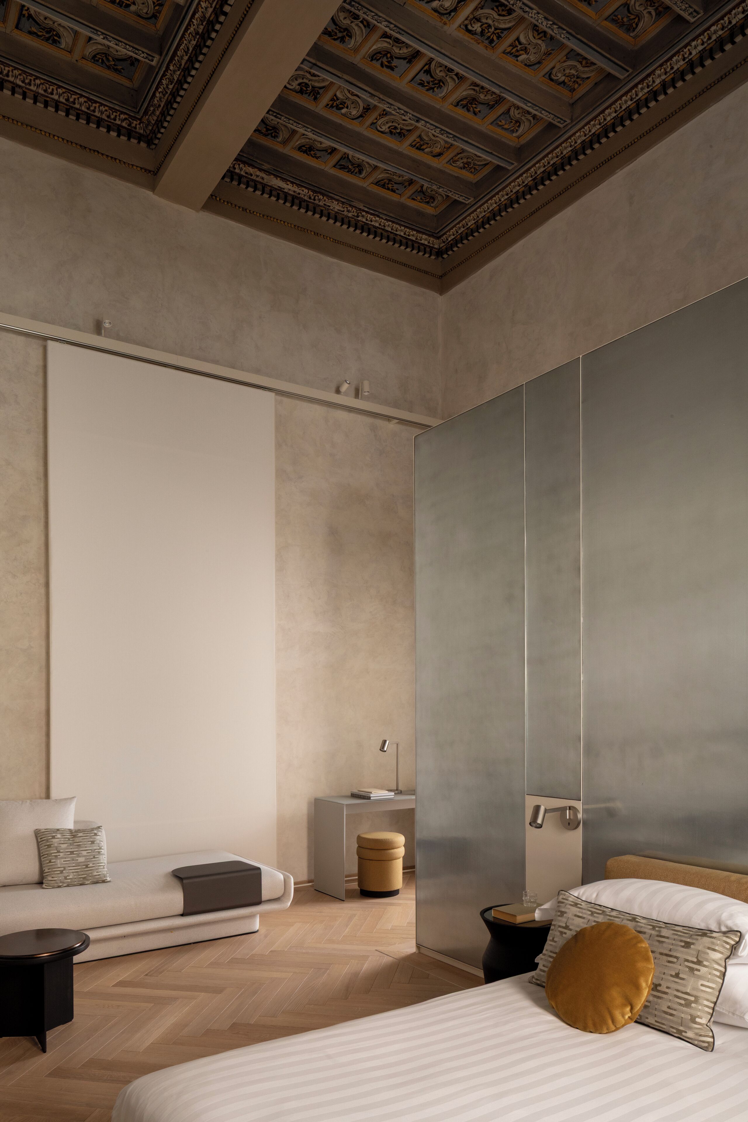Un dormitorio moderno con una cama grande, un sofá, una mesita de noche y un techo decorativo.
