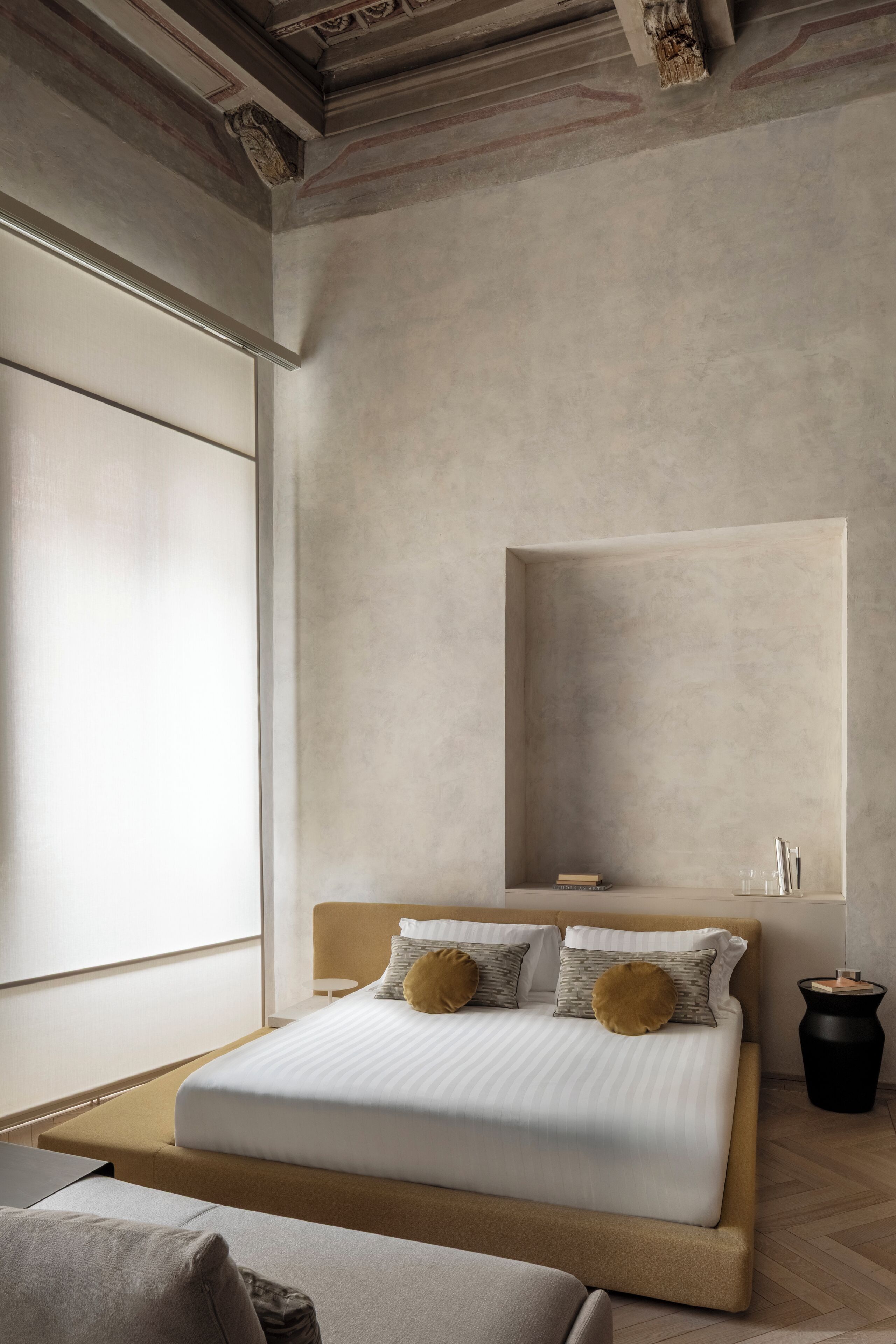 A modern hotel room with a large bed, a bedside table, a small desk, and a window with blinds.