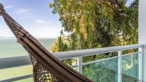 A hammock on a balcony overlooking a body of water and dense foliage. - Loft em Condom nio com mar em Mangaratiba (Mangaratiba)