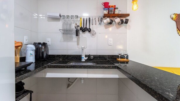 A kitchen with a granite countertop, a stainless steel sink, and a hanging utensil rack. - Loft em Condom nio com mar em Mangaratiba (Mangaratiba)
