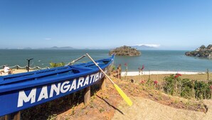A blue boat named 'MANGARATIBA' docked at a beach with a clear view of the ocean and distant islands. - Loft em Condom nio com mar em Mangaratiba (Mangaratiba)