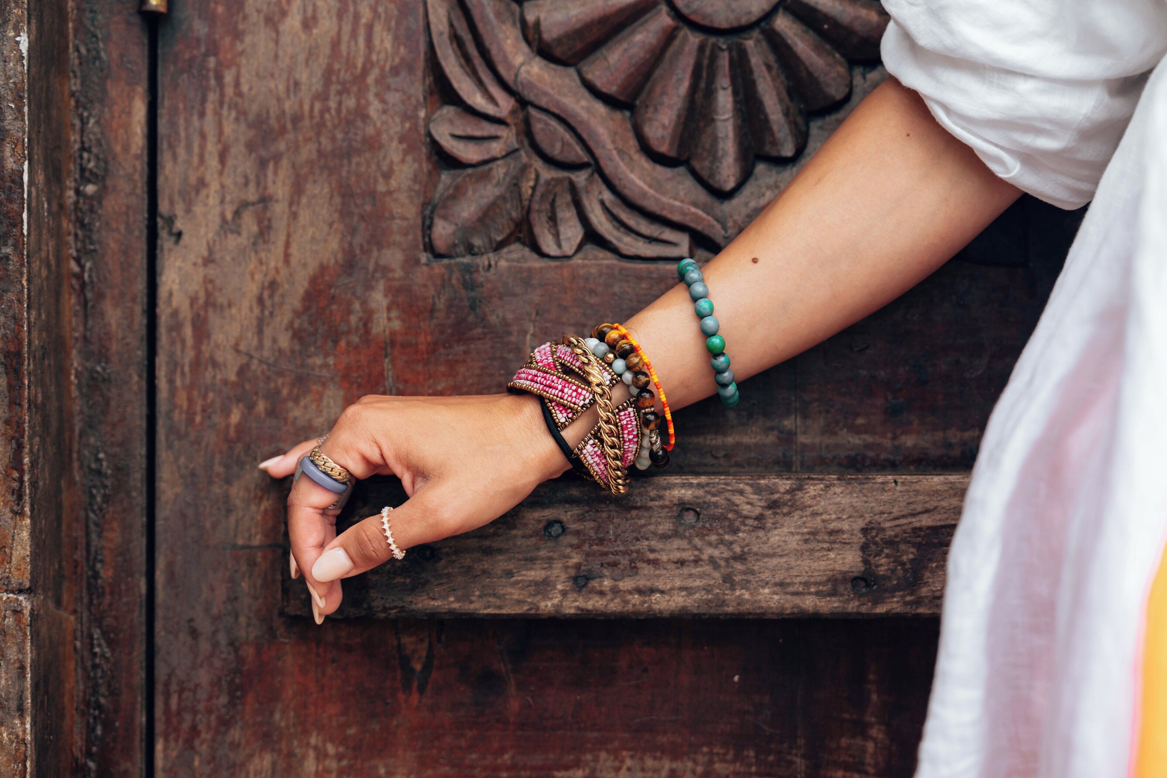 A hand resting on a wooden surface with a carved design, wearing multiple bracelets and rings.