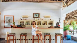 A bar area with wooden stools, a bar counter, and various bottles. - Hekaya Zanzibar (Michamvi)