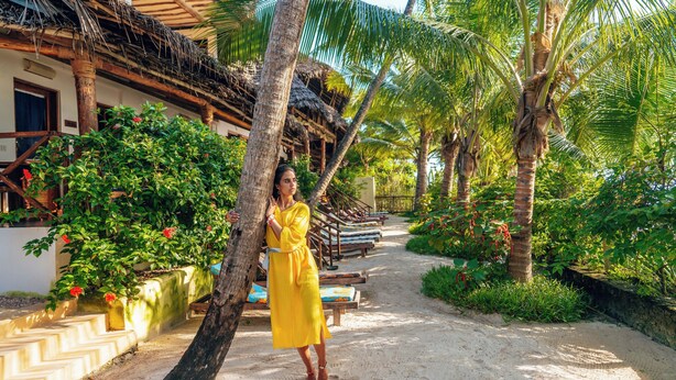 A tropical resort with a thatched-roof building, palm trees, and a sandy pathway. - Hekaya Zanzibar (Michamvi)