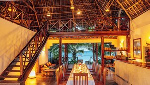 A dining area with a view of the ocean, wooden furniture, and a staircase leading to an upper level. - Hekaya Zanzibar (Michamvi)