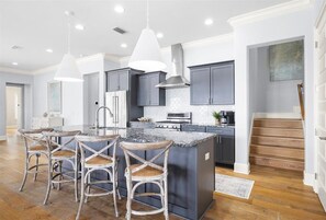 Uma cozinha com ilha central, banquetas, iluminação pendente e uma escada que leva a outro nível.