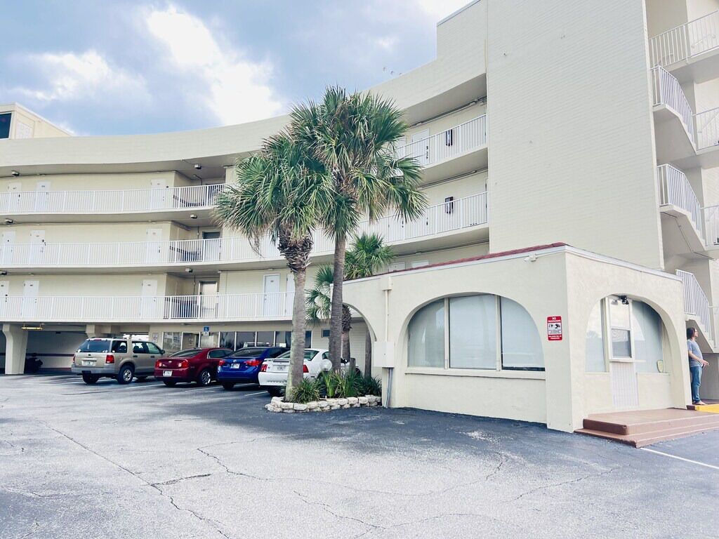 A multi-story building with a parking lot, several cars, and a palm tree.