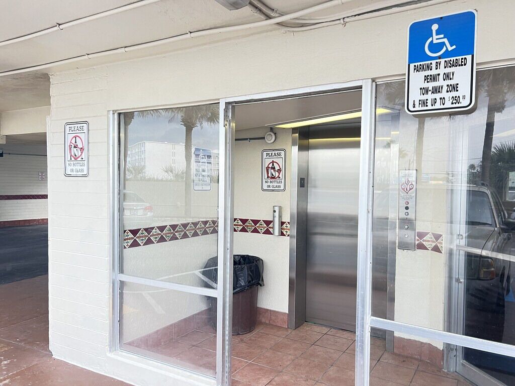 A building entrance with a no-bottles sign, a disabled parking sign, and an elevator.