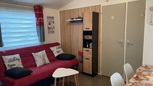 Een ruimtelijk ingerichte woonruimte met een rode bank, een kleine eettafel en een kitchenette.
