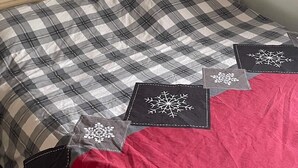 Een bed met een geruit sprei en decoratieve kussens, een nachtkastje met een lamp en een wandplank.