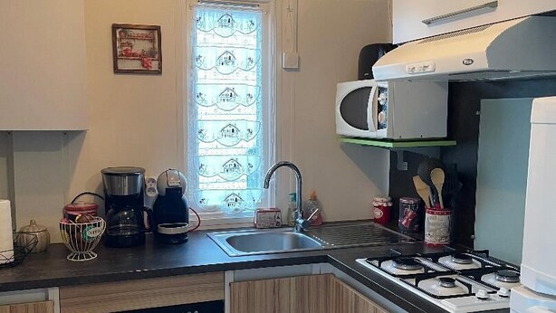 Een kleine keuken met een vaatwasser, een magnetron, een gasfornuis en een spoelbak.