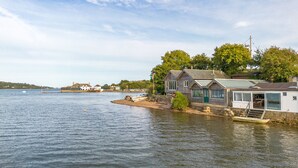 En ejendom ved vandet med en dock, en lille båd, og et hus med store vinduer og en overdækket veranda.