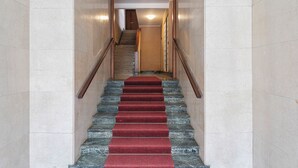 A staircase with red carpeted steps leading to a wooden door at the top. - Quinto Modern Flat by Wonderful Italy (Genoa)